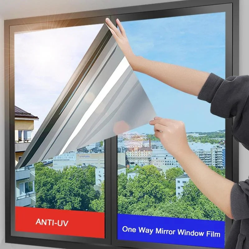 A hand is applying a one-way mirror window film to a glass pane, demonstrating its installation.