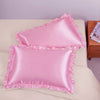 A set of two pink ruffled satin pillowcases with silky envelope closures resting on a light-colored surface.
