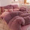 A pile of fluffy mauve mink velvet bedding and pillows on a bed.
