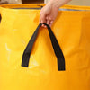A hand is opening a bright yellow heavy duty waterproof storage bag by pulling a black strap.