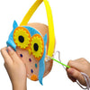 A hand is using a plastic sewing needle with a large eye to work on a colorful felt owl craft.