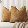 A close-up of two textured, golden brown chenille throw pillows resting on a light-colored fabric.