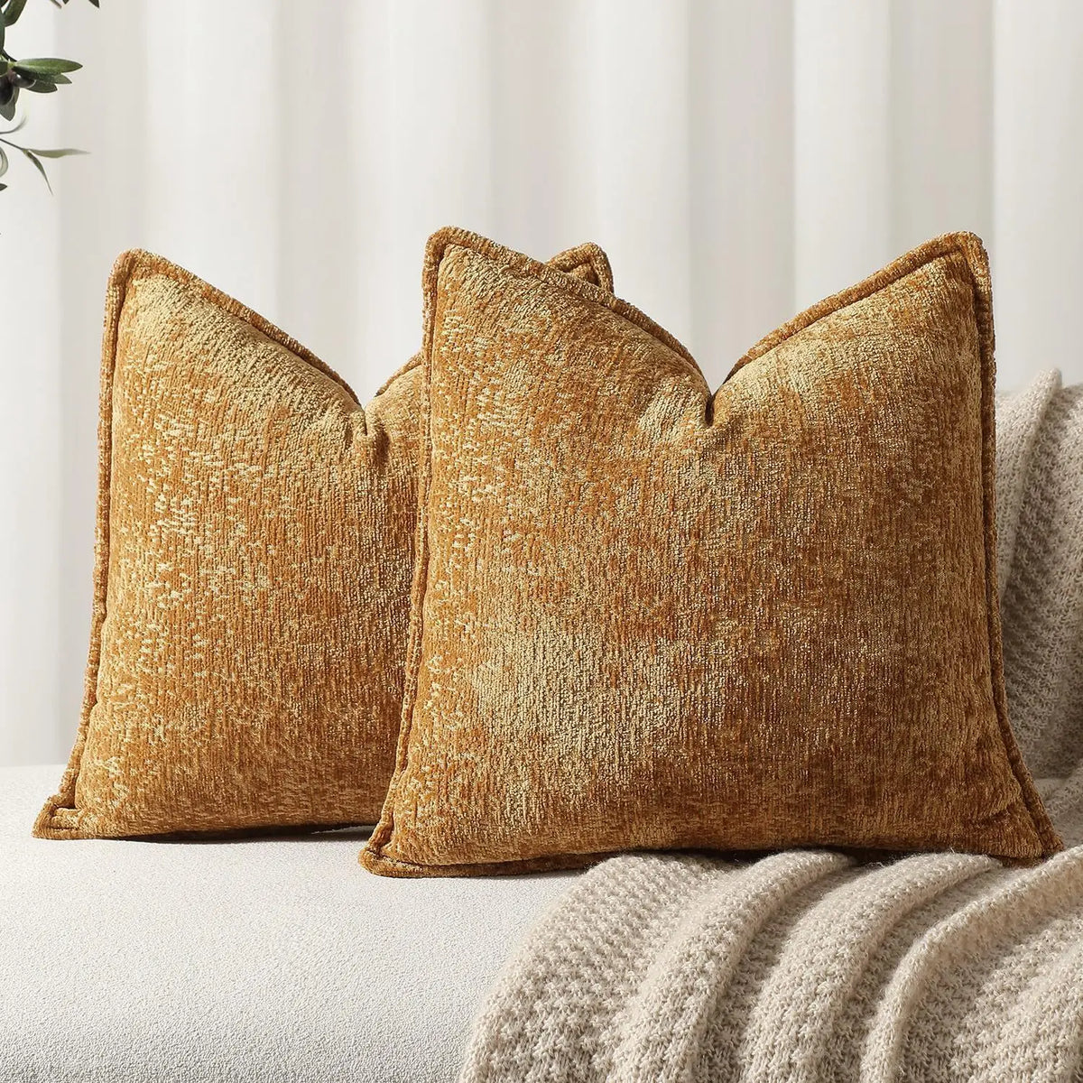 A close-up of two textured, golden brown chenille throw pillows resting on a light-colored fabric.