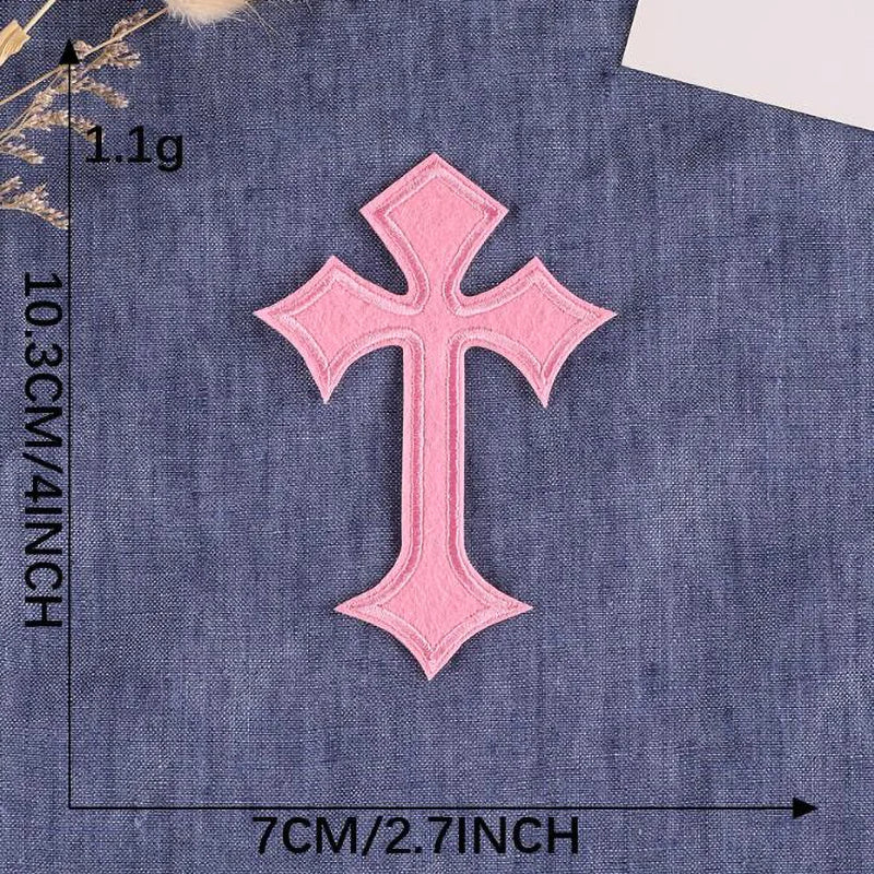 A pink cross embroidery patch on a dark blue fabric background.