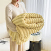 A person is holding a large, fluffy, pale yellow plush blanket with thick, ribbed texture.