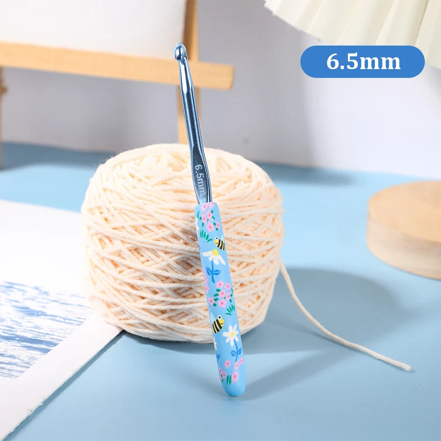 A blue ergonomic crochet hook with a floral design is shown next to a ball of light-colored yarn.