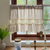 Beige gingham crochet lace curtain valance hanging in a window with greenery and light