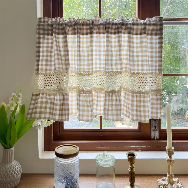 Beige gingham crochet lace curtain valance hanging in a window with greenery and light
