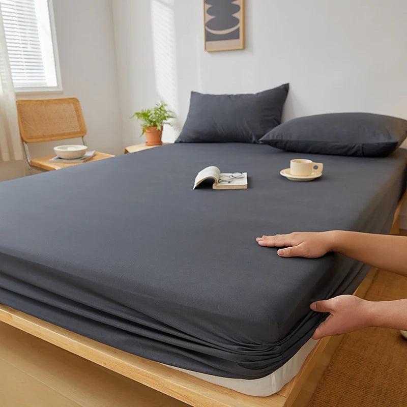 A dark gray fitted sheet is draped over a wooden bed frame, showing its deep pockets and elastic edges.