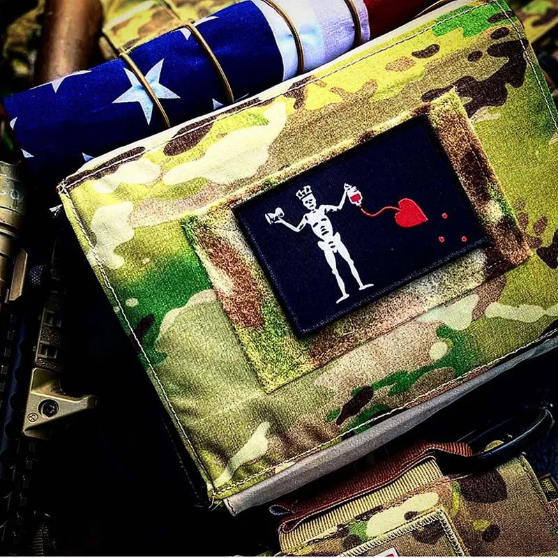 A pirate flag embroidered patch featuring a blackbeard skull, hook, and loop backing on camouflage fabric.