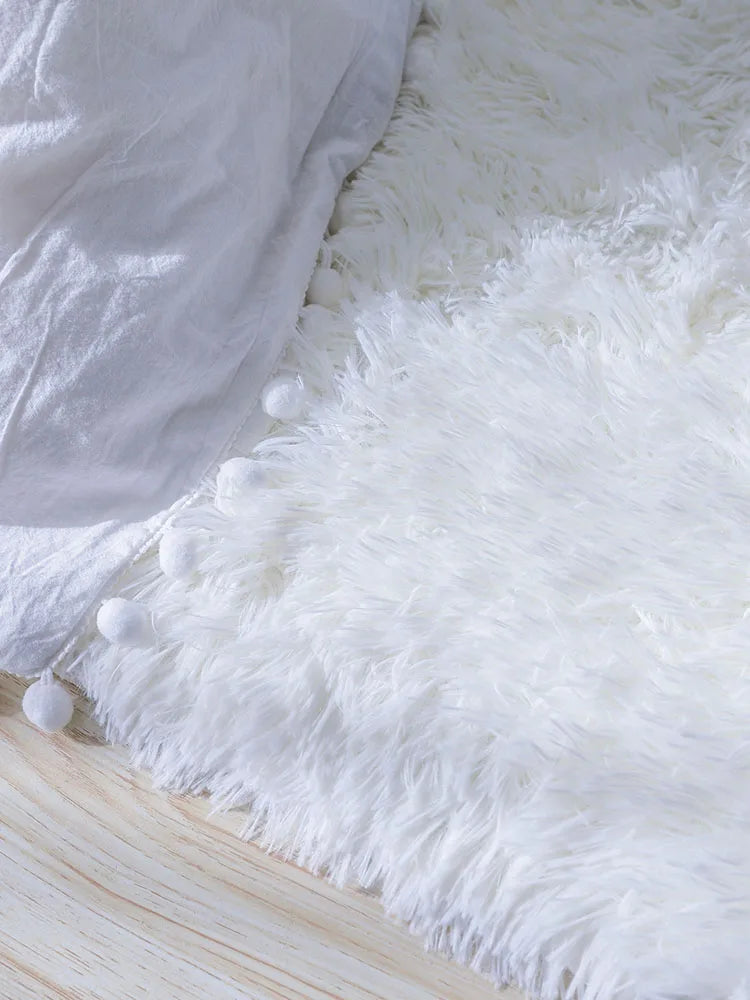 A fluffy white shag rug placed on a wooden floor next to a white fabric item.