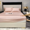 A pink fitted sheet and pillow set displayed on a bed with a black headboard and white bedding.