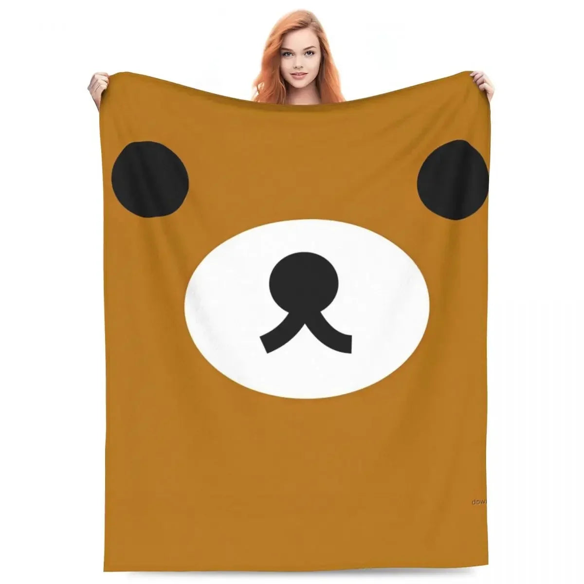 A brown cartoon bear face design on a tan throw blanket.
