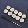 A set of adjustable metal snap buttons with white and yellow daisy patterns arranged on a dark blue fabric.