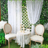 A set of vintage floral lace curtains framing a garden scene with white chairs and greenery.