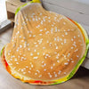 A plush throw blanket shaped like a pizza with a golden crust and white sesame seeds.