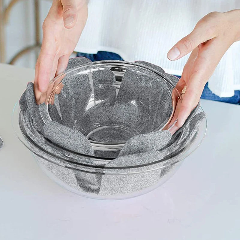 Hands are placing reusable felt pot protectors into a clear glass bowl for kitchen storage.