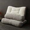 A stack of three beige quilted ergonomic contour pillows for neck and spine support resting on a gray carpet.