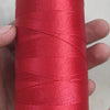 A spool of bright red high tenacity polyester sewing thread is held in a hand, with the yellow core visible.