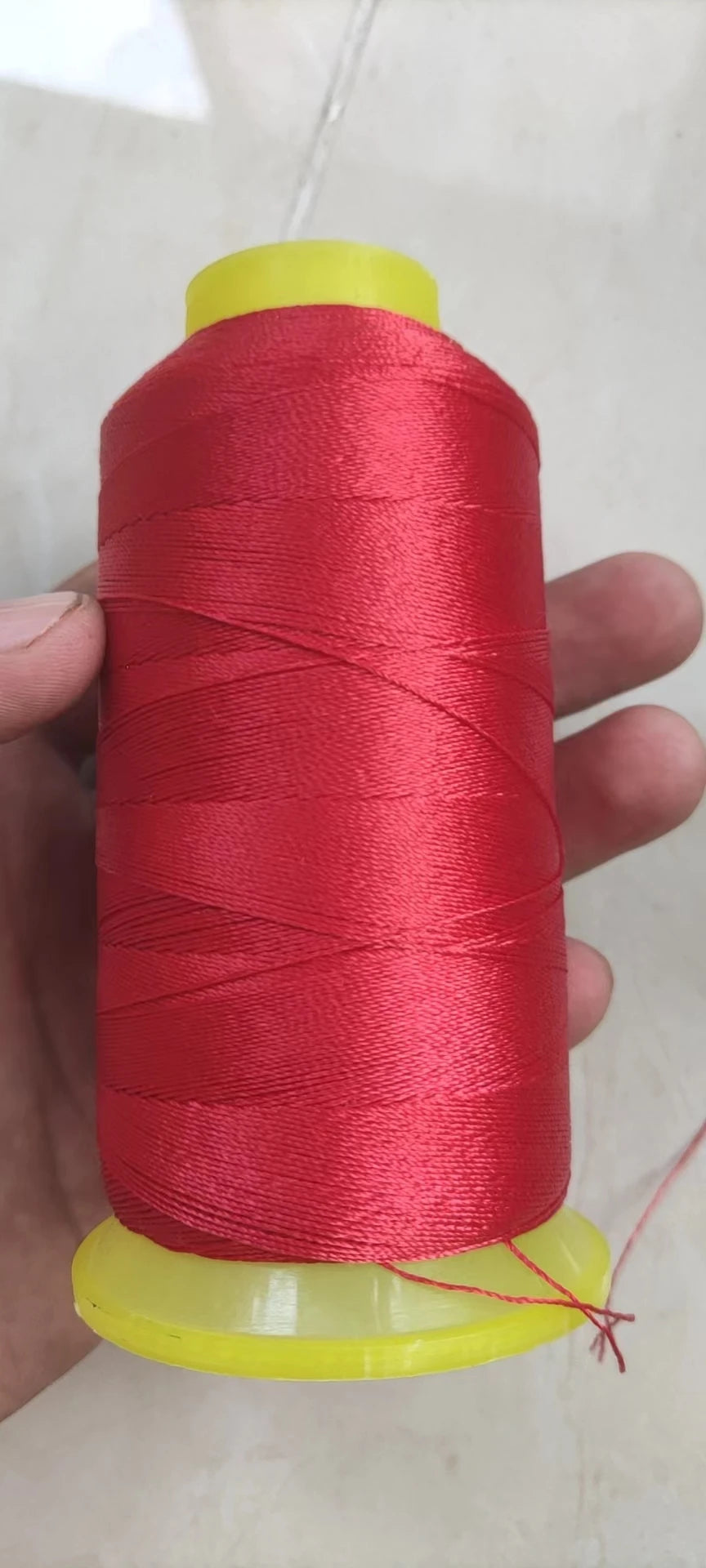 A spool of bright red high tenacity polyester sewing thread is held in a hand, with the yellow core visible.