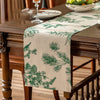 A beige table runner with a green fern pattern is placed on a dark wooden dining table.