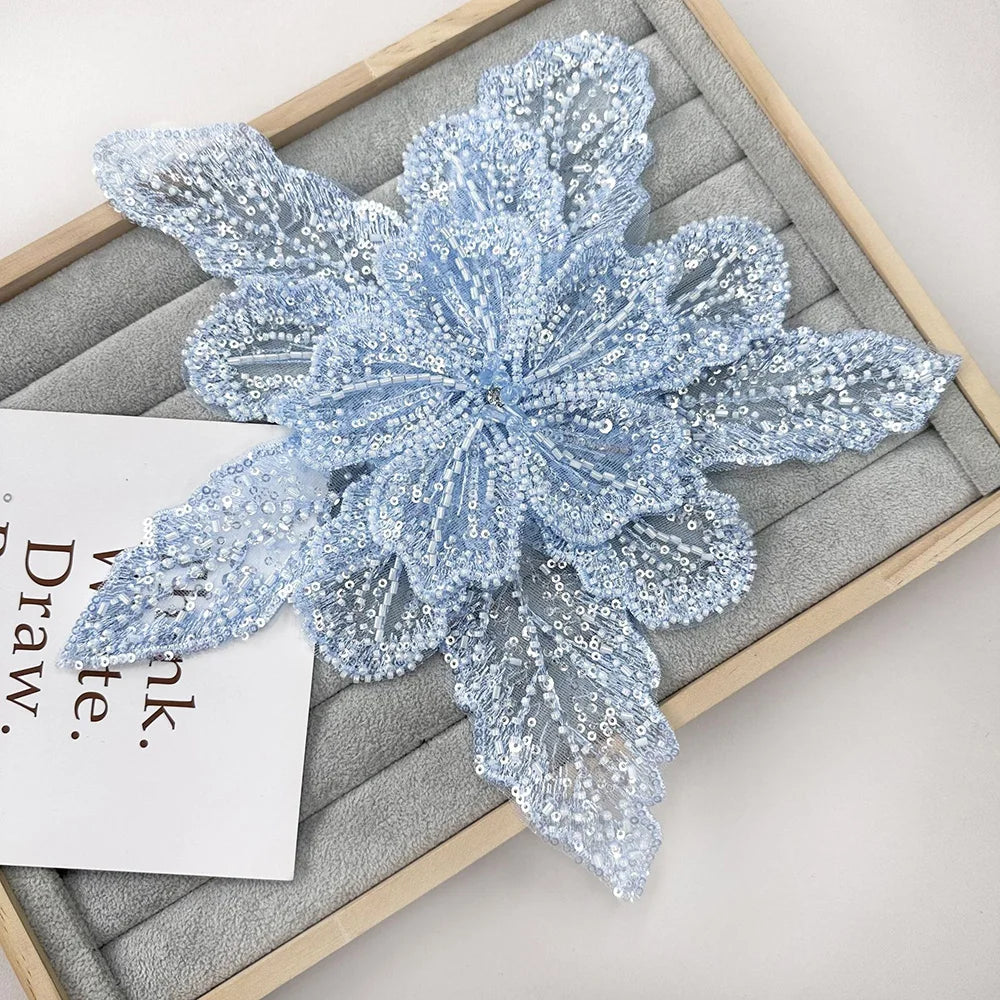 Light blue floral lace applique fabric patches with sequins displayed on a wooden tray.