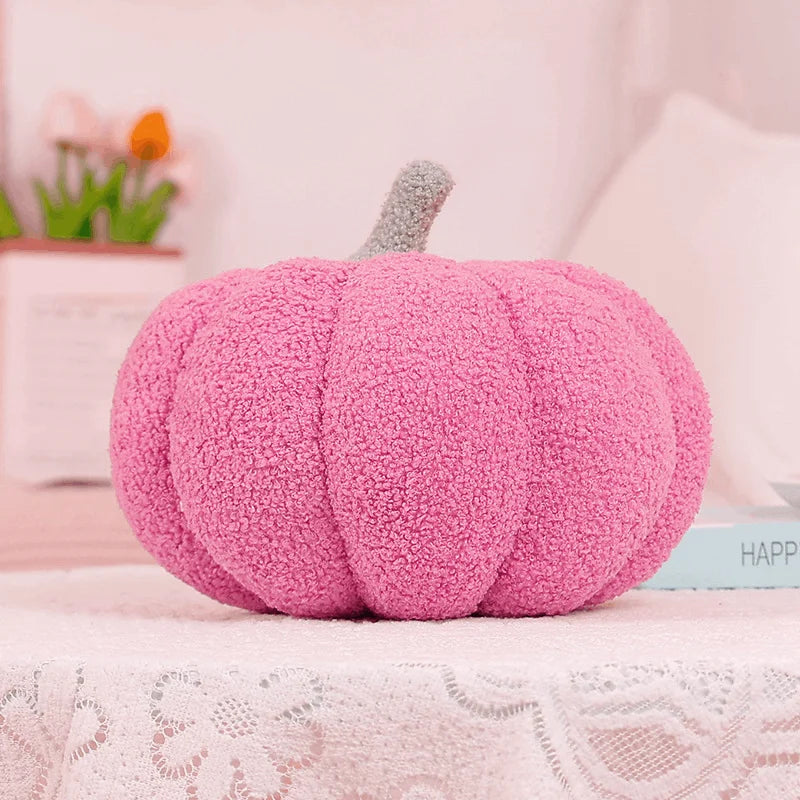 A fluffy pink pumpkin shaped throw pillow with a gray stem resting on a white lace surface.