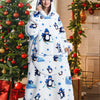 A woman wearing a white sherpa fleece oversized blanket hoodie with blue penguin patterns in a festive holiday setting.