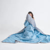 A person is lying down under a light blue cooling blanket, looking up through the fabric.