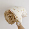 A rolled muslin blanket with a floral print is shown against a light background.