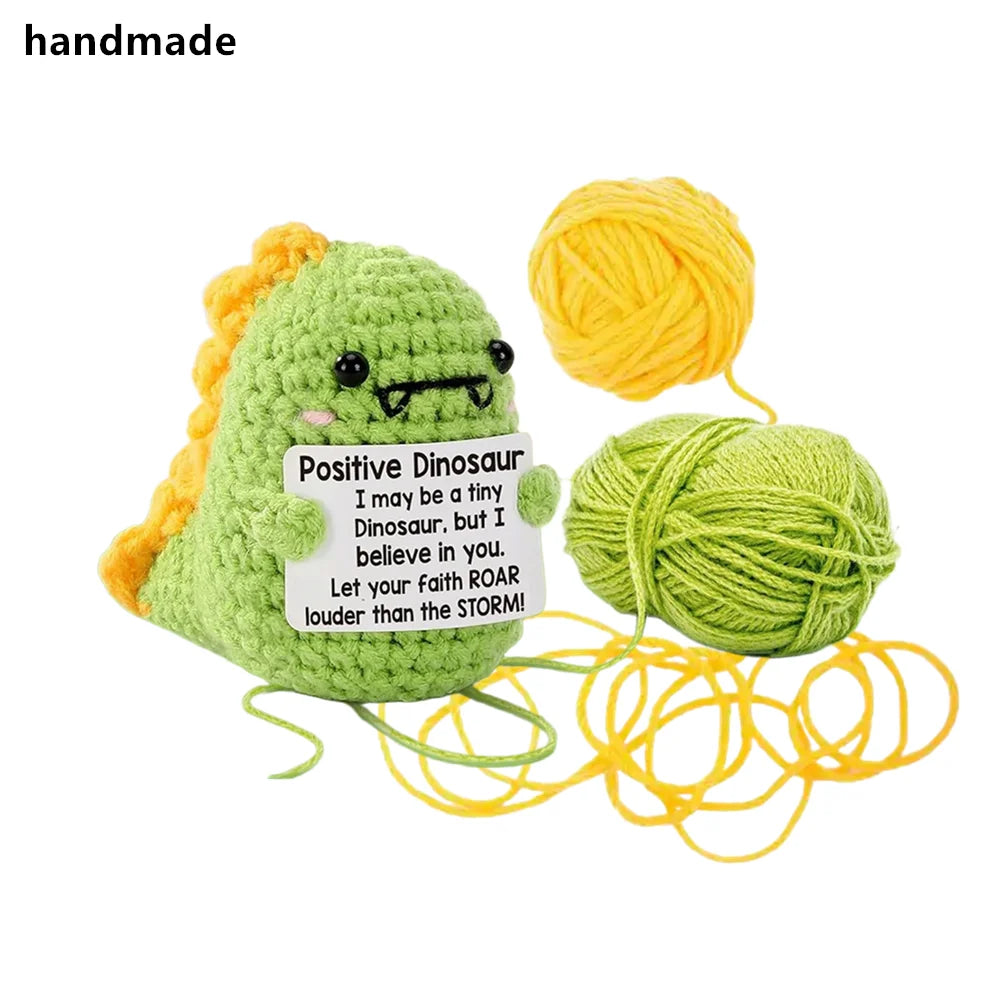 Handmade plush dinosaur toy made of green yarn with a yellow yarn ball nearby