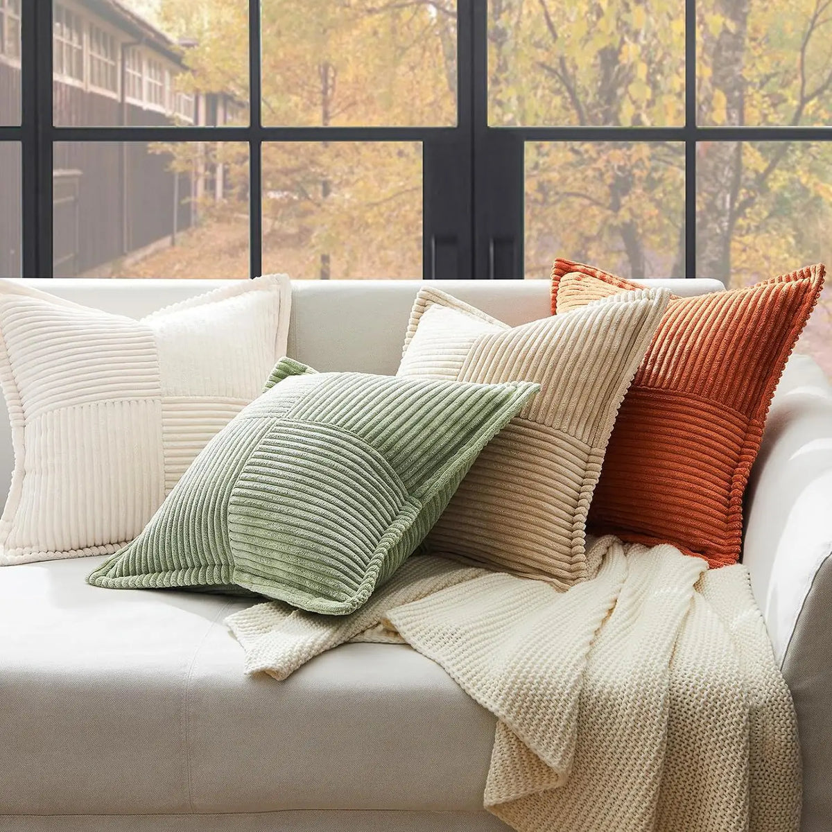 A collection of striped corduroy lumbar support pillows in cream, olive green, and burnt orange resting on a white sofa.