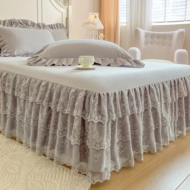 A bed dressed with a sheer gray lace ruffled skirt and matching pillow covers in a bedroom setting.