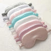 A set of five pastel colored silk sleep masks arranged in a row on a white surface.