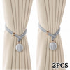 A pair of silver rope tiebacks with gold accents displayed against a light beige curtain.