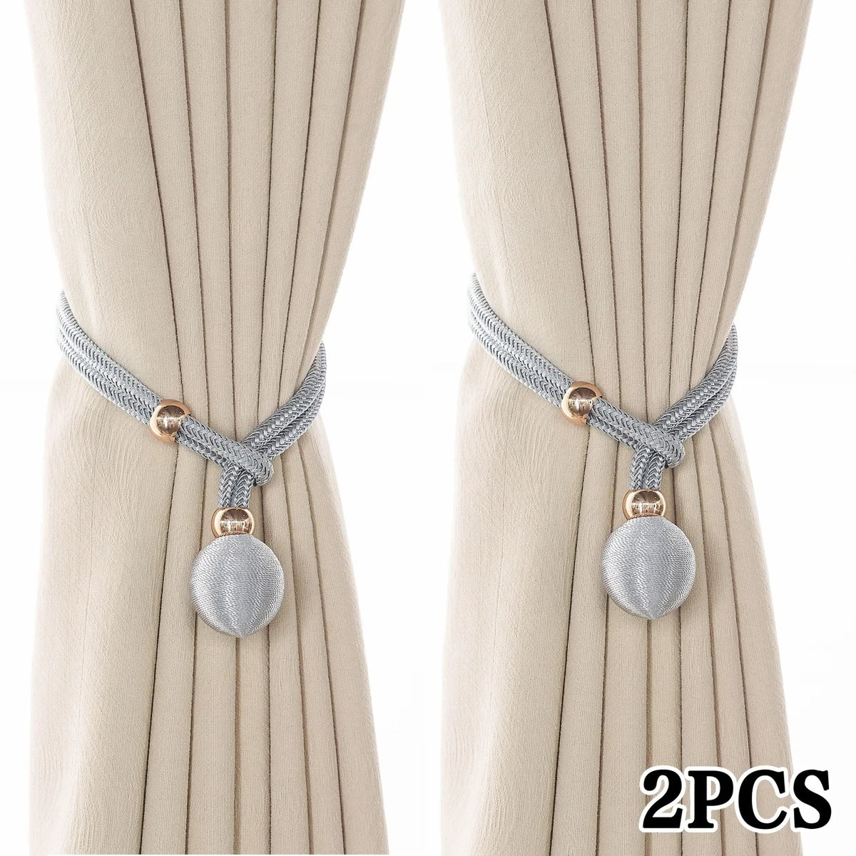 A pair of silver rope tiebacks with gold accents displayed against a light beige curtain.
