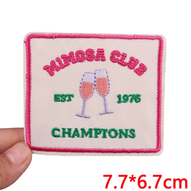 Pink embroidered patch with purple text and a crown design featuring the words Mimosa Club Est 1976 Champions