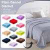 A variety of plain flannel blankets in pink, purple, red, blue, gray, and olive colors displayed next to a white bed.