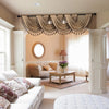 Elegant beige window curtain valance with tassels hanging over a window in a softly lit room.