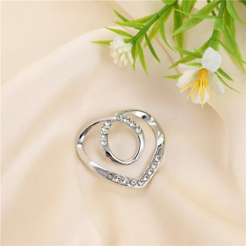 Silver metal ring clips with small diamonds resting on a soft beige fabric next to green foliage.