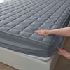 A hand is touching a gray quilted waterproof mattress protector on a bed.