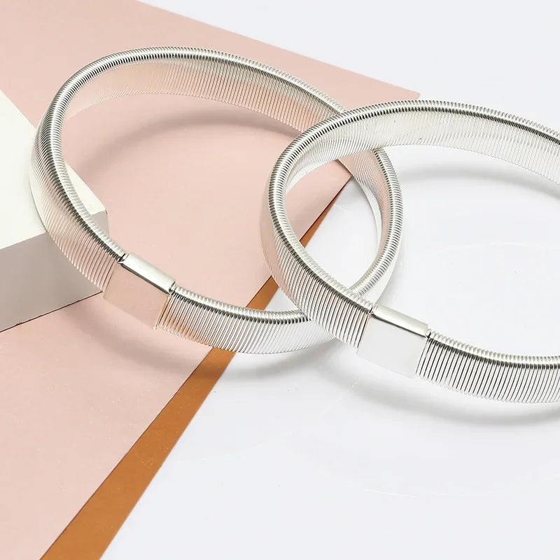 Silver metal sleeve garters or adjustable arm bands lying on a pink and brown surface.