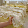 A hand is holding a light yellow summer floral print quilt blanket with delicate lace trim.