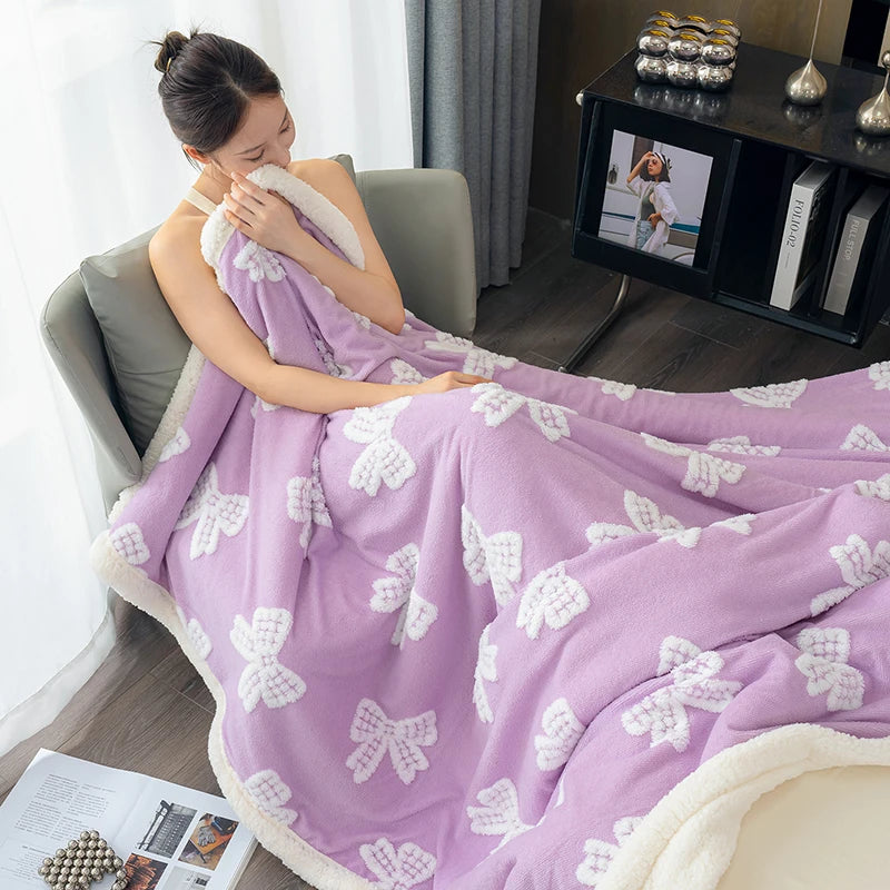 A purple lambswool blanket with white floral embroidery is draped over a person in a modern indoor setting.