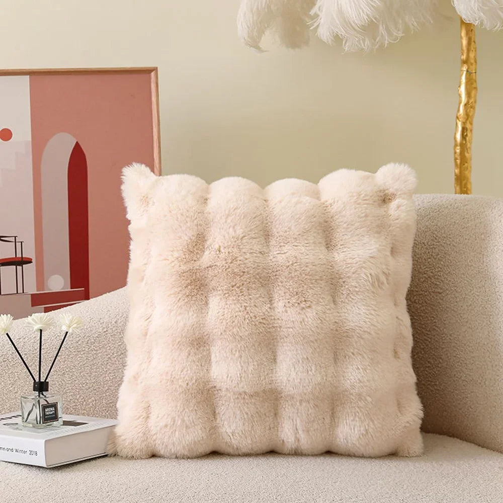 A fluffy beige plush cushion cover resting on a light-colored sofa.