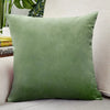 A square velvet cushion cover in a muted olive green color resting on a light-colored sofa.