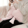 A person is holding a pink fluffy decorative bow pillow in a light beige sweater while sitting down.