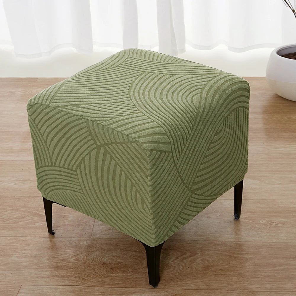 A square ottoman slipcover in olive green features a geometric, wavy pattern on a wooden floor.