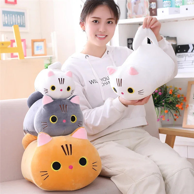 A young woman is holding a white cat plush pillow and a gray cat plush cushion in a bright indoor setting.