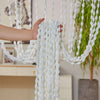 A hand is pulling a white decorative fabric door curtain with tassel trim, featuring numerous white pom-poms.